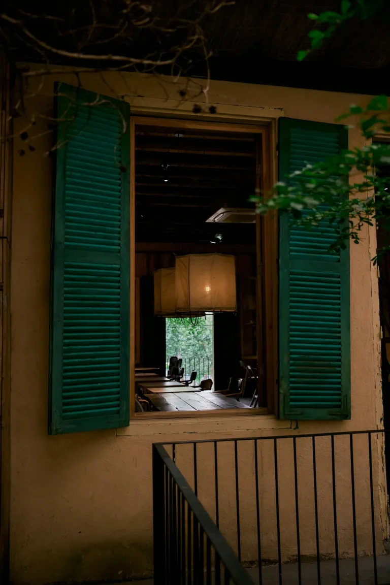 Green shutters open on a window lit by a lantern