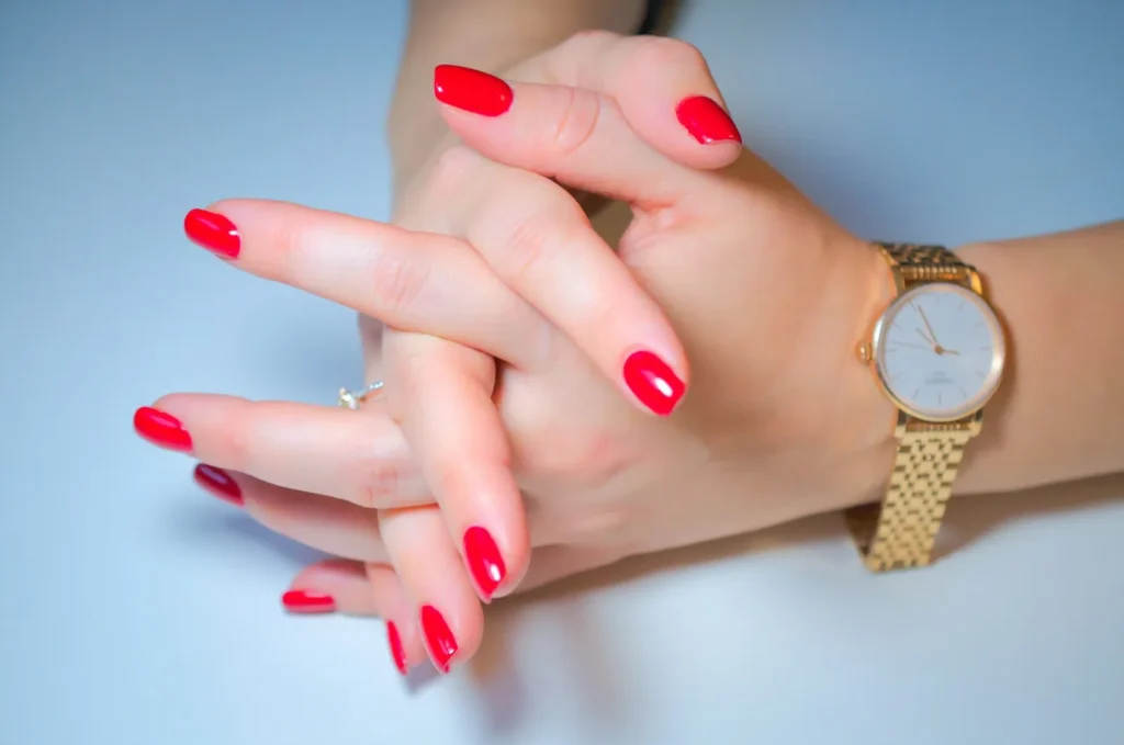 Red nails and a gold watch on blue