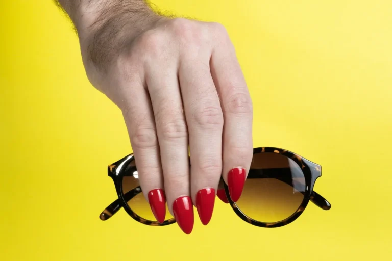 Red nails holding sunglasses on yellow